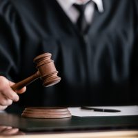 partial view of blurred judge in robe holding gavel in court partial view of blurred judge in robe holding gavel in court